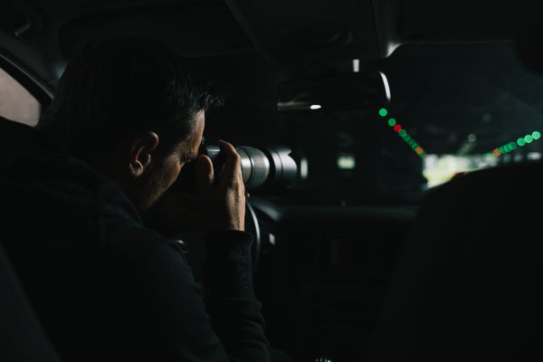 Detectives privados; vista trasera de un hombre haciendo vigilancia con cámara digital.
